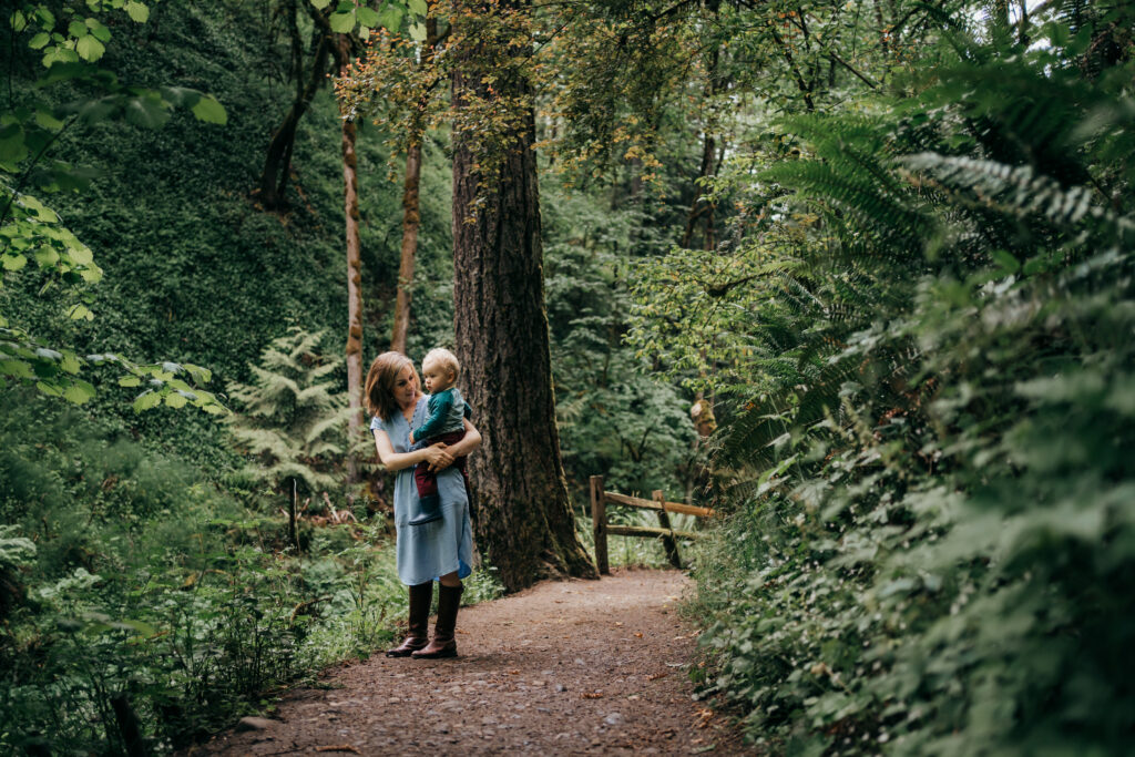 mom holding her baby and showing trees on a Portland hike trail