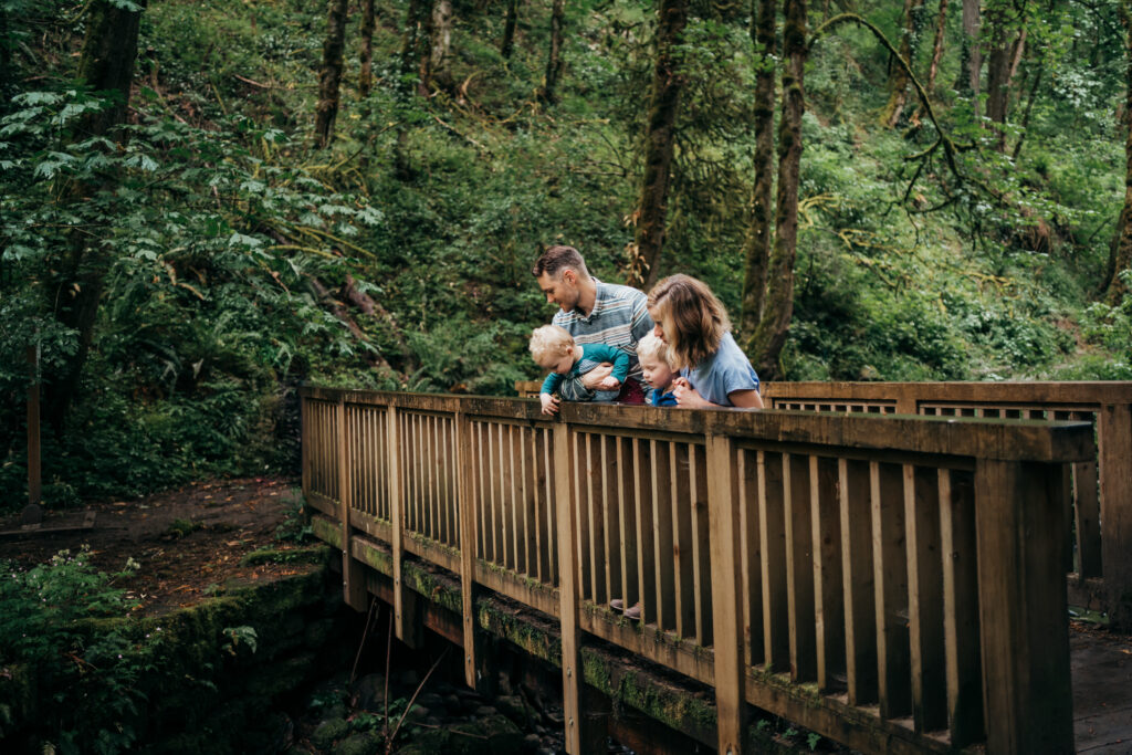 family of four looking into river from a wooden bridge on hike trail in Portland