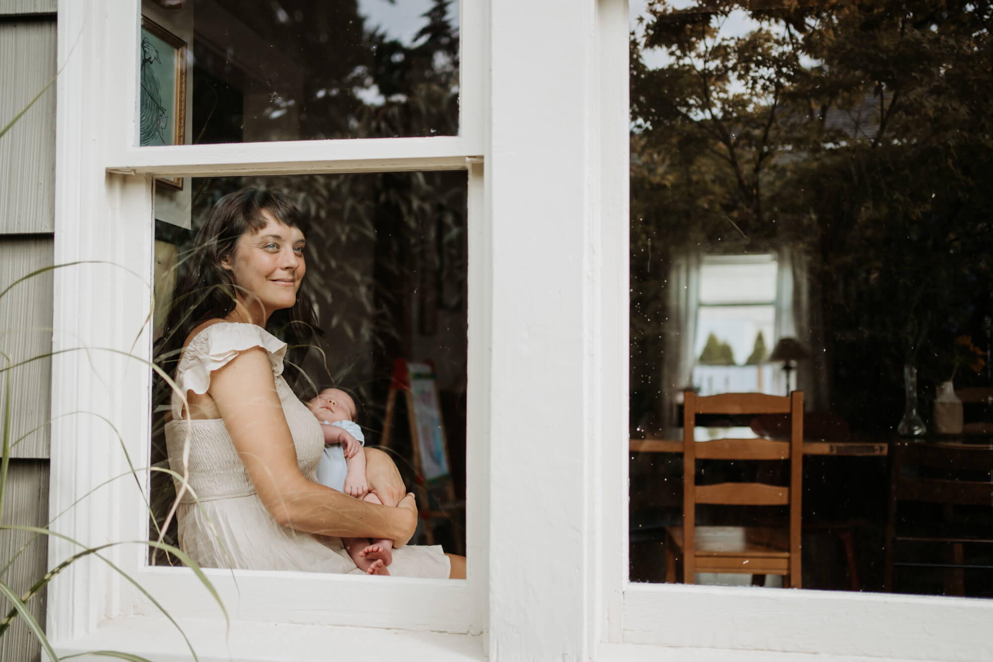 Mom holding her newborn baby by the window and looking outside smiling