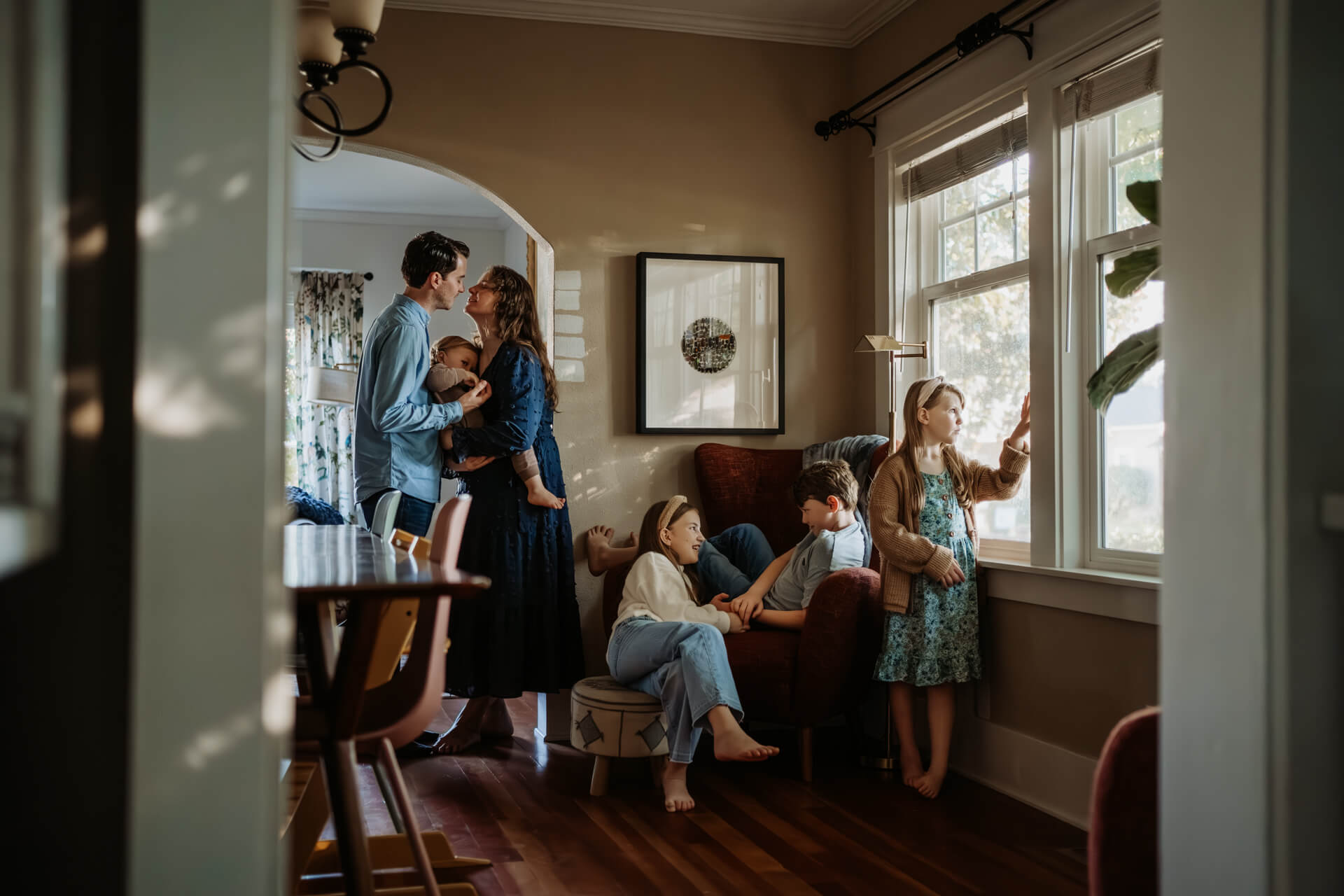 Family of 6 hanging out and playing in a dining room by the window in their home in Portland, OR