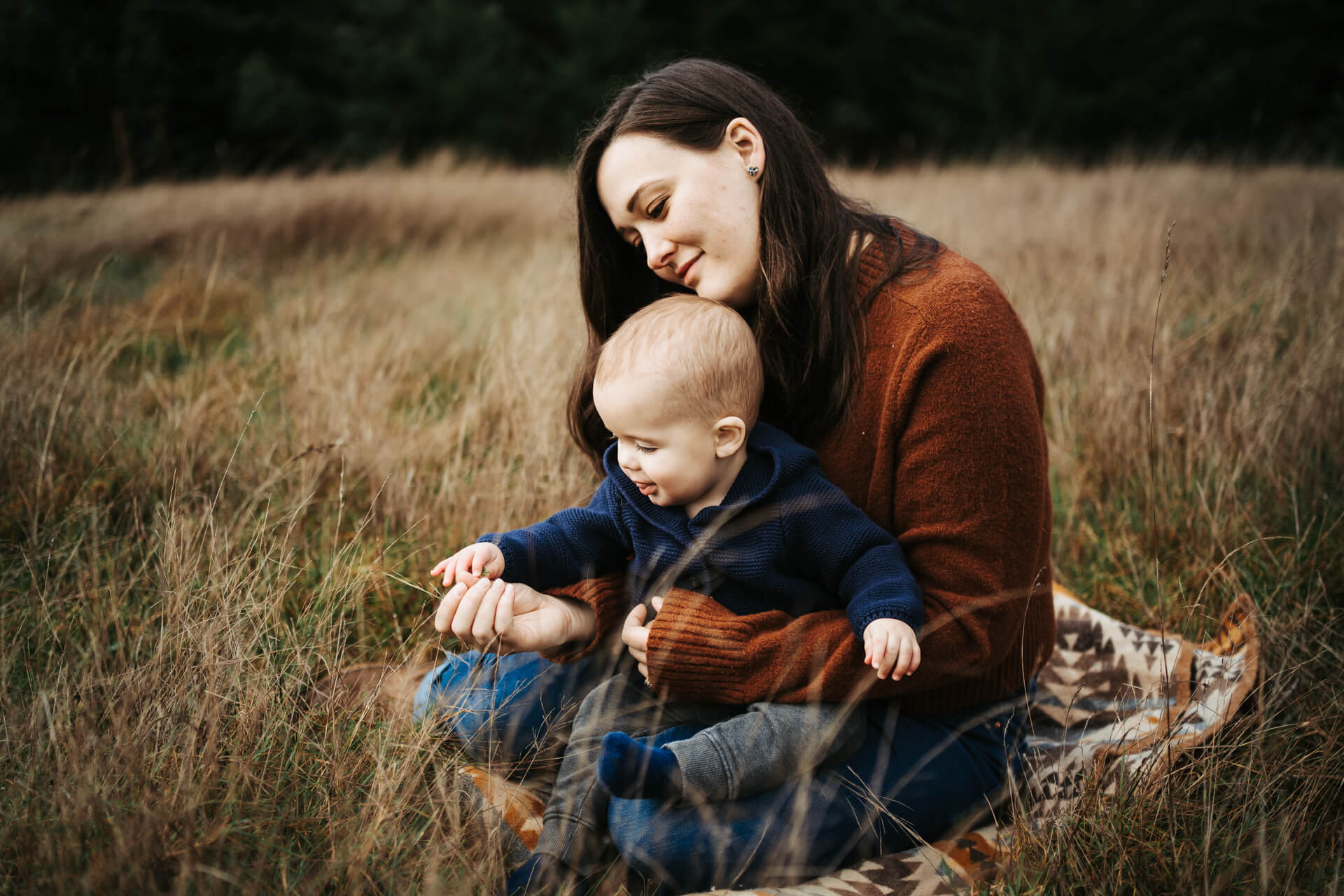 Mom and her baby sitting on a golden grass field and playing with grass