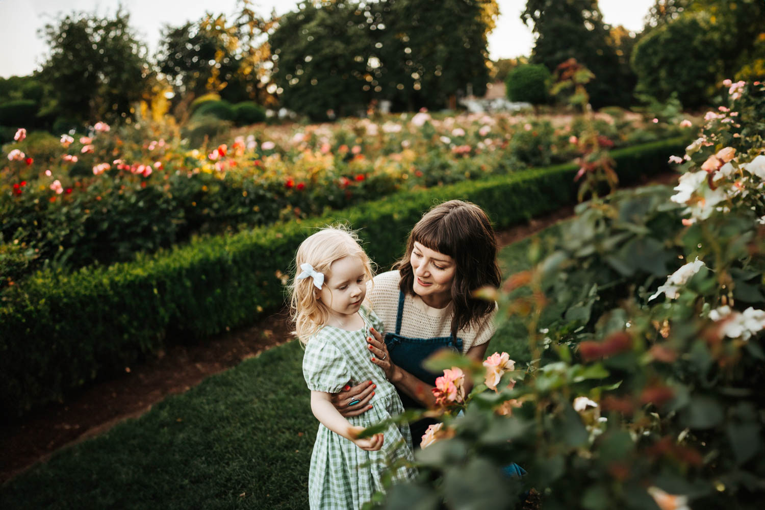 Mom and her toddler daughter looking at flowers in a park in Portland, OR