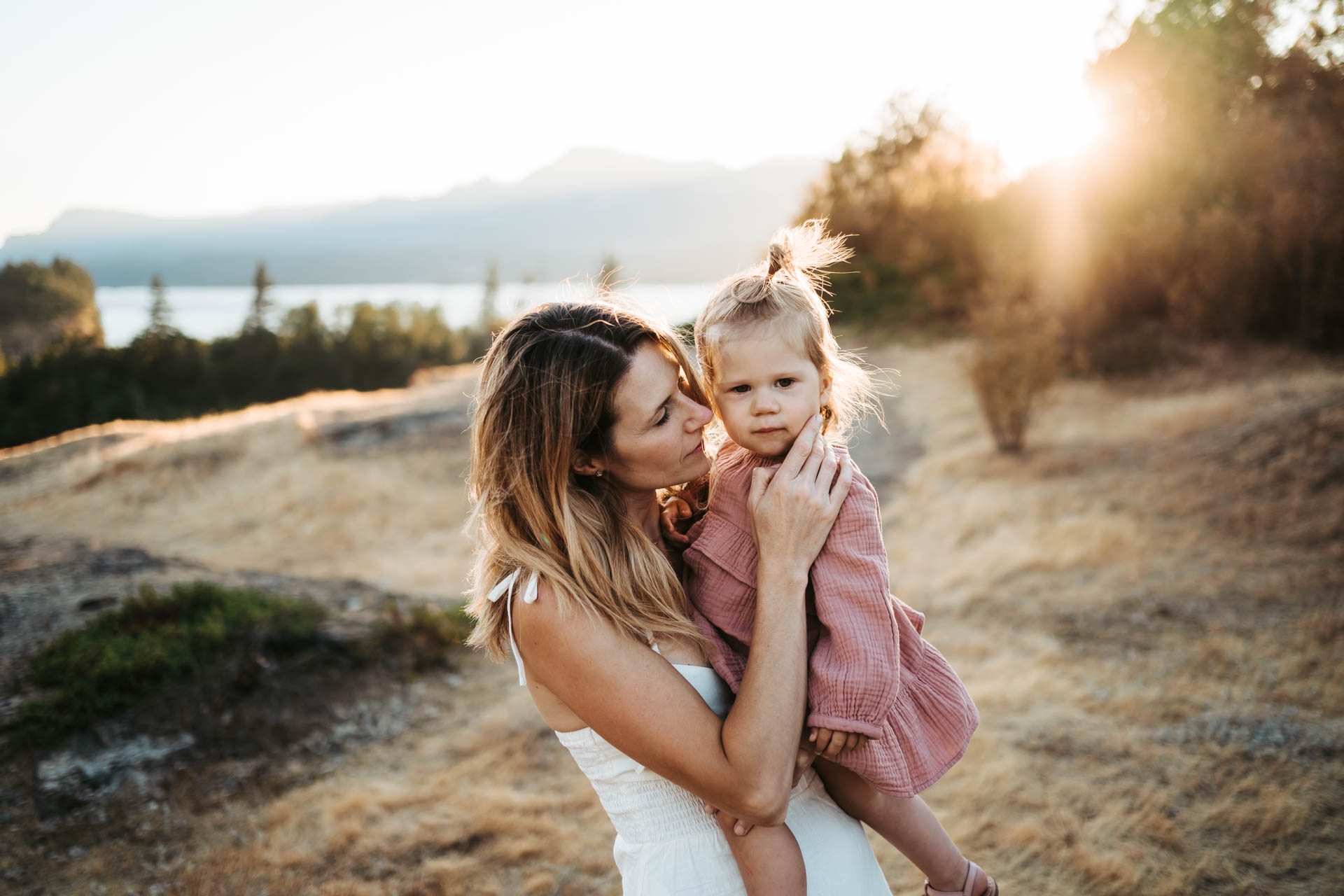 A mom holding her toddler and touching her cheeks in a grass filed in golden light