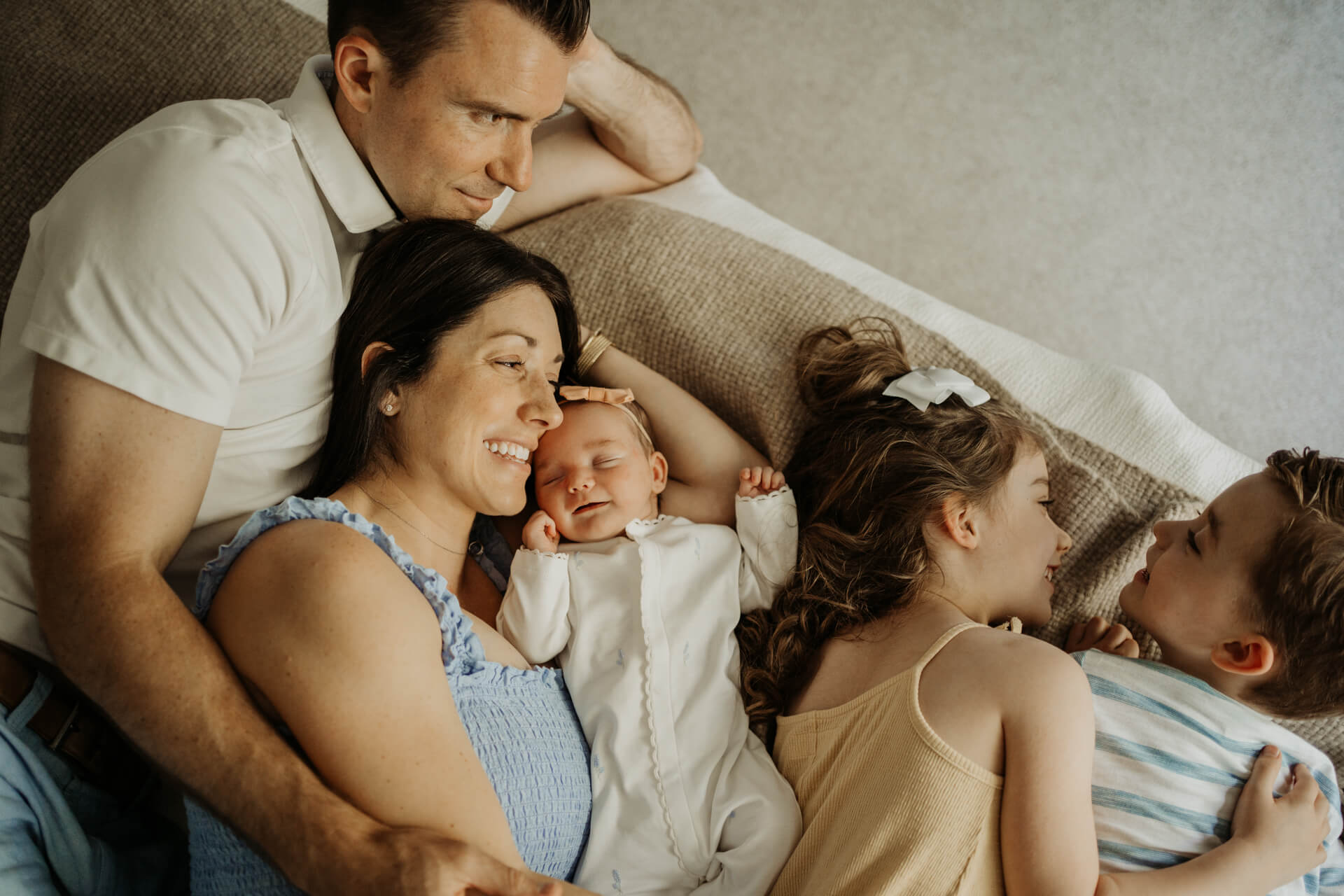 Happy Family of 5 including a newborn baby girl and 2 toddlers are laying down on the be togather