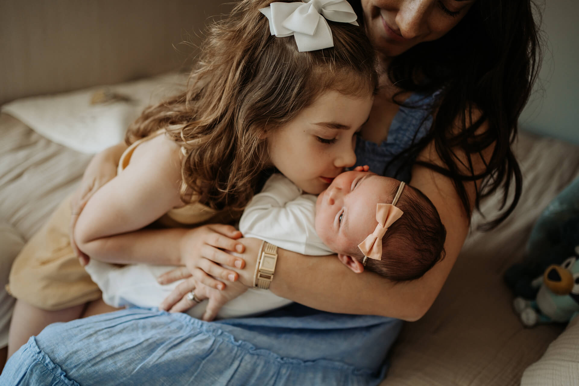 Toddler girl giving a kiss to her newborn baby sister on her cheek