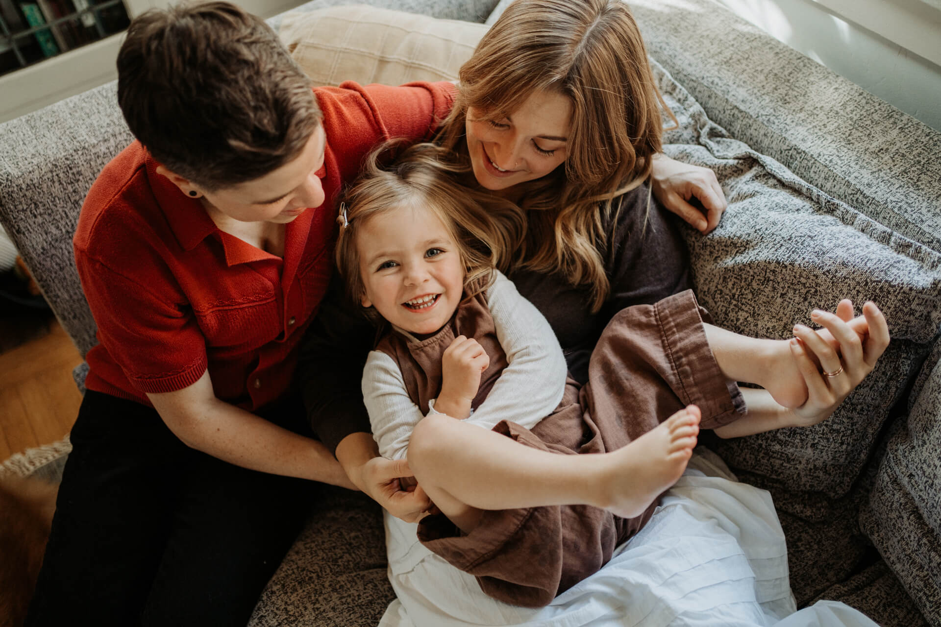 joyful in-home family photography session in Portland featuring parents cuddling their toddler on the couch
