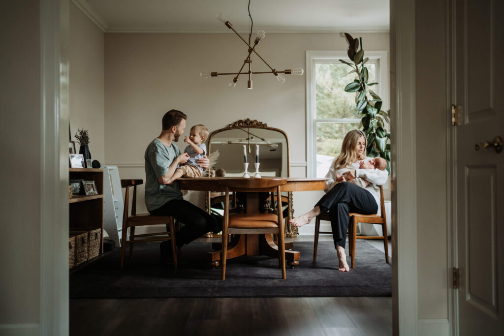 Lifestyle in-home family photo session in Portland, OR with parents, toddler, and newborn gathered together at the dining table