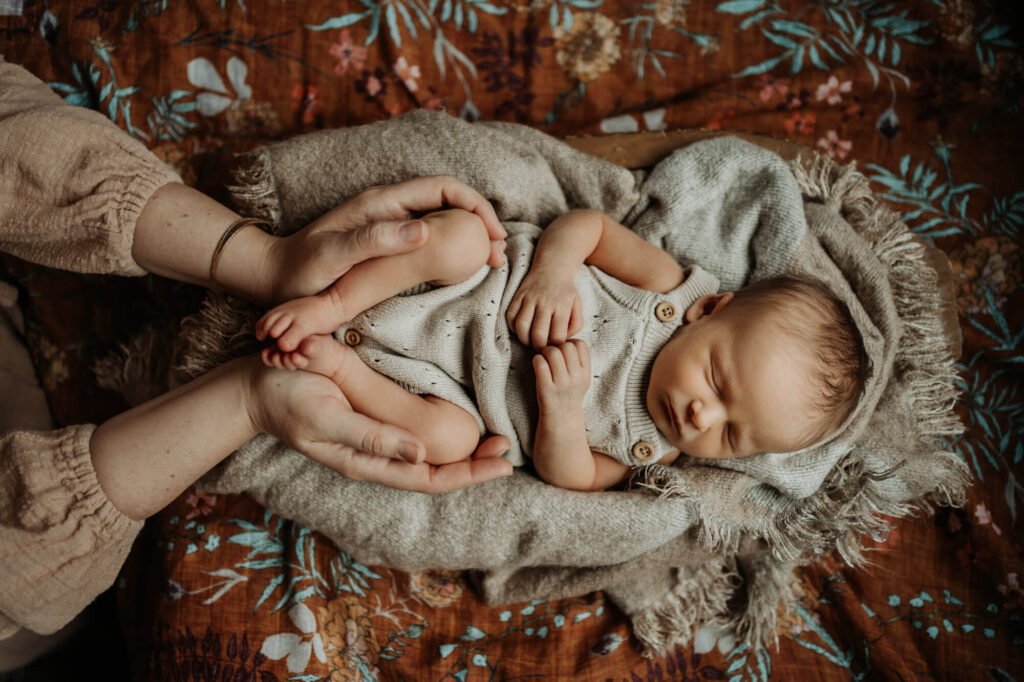 Sleeping newborn held gently in parents’ hands during an in-home newborn photography session in Portland, Oregon